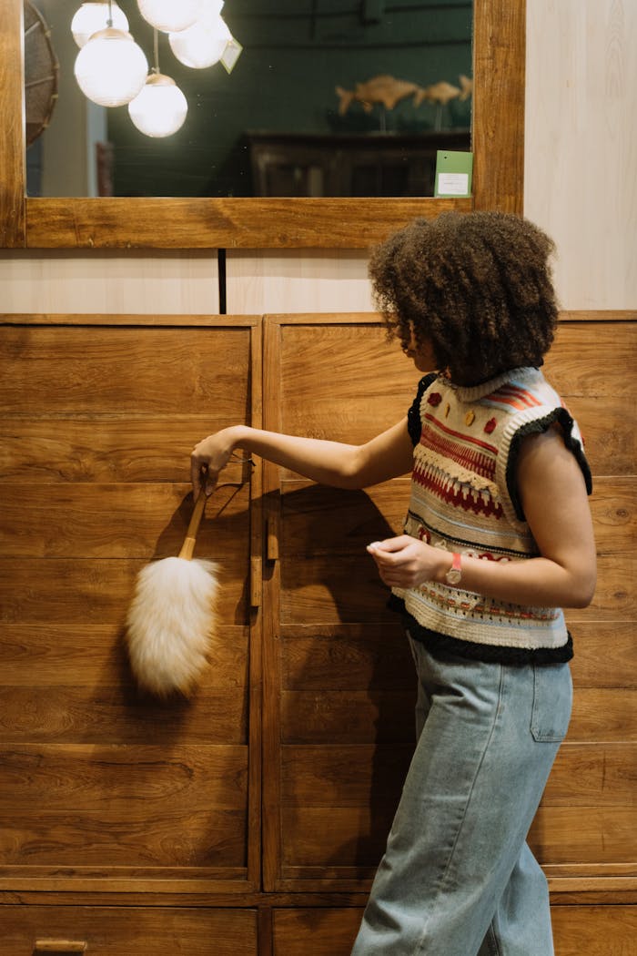 Woman using a duster to clean a wooden cabinet indoors, showcasing an active cleaning routine.